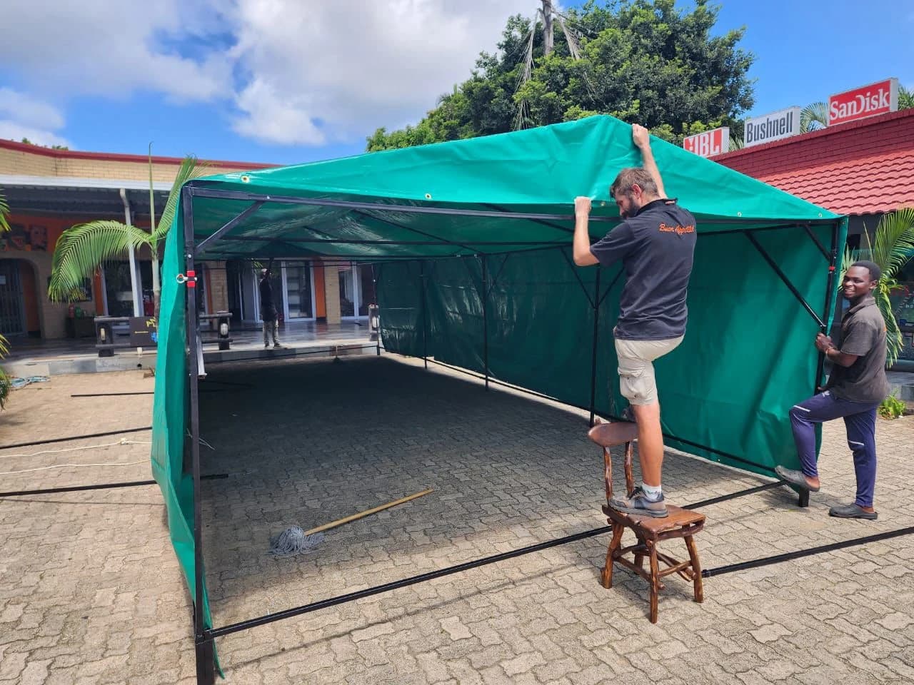 Minurphy team fitting a custom green PVC event canopy at a shopfront, showing trade labour and installation finishing
